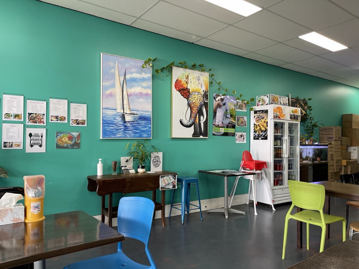 The dining room: turquoise walls with framed pictures, blue and green chairs, small tables and a drinks fridge