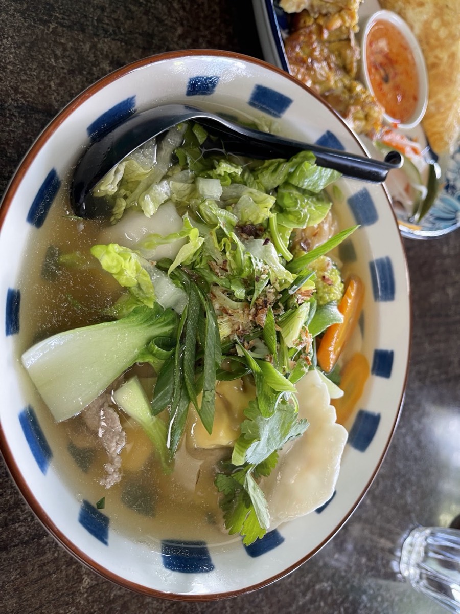 A blue-rimmed bowl of clear soup with leafy greens, herbs and pale dumplings